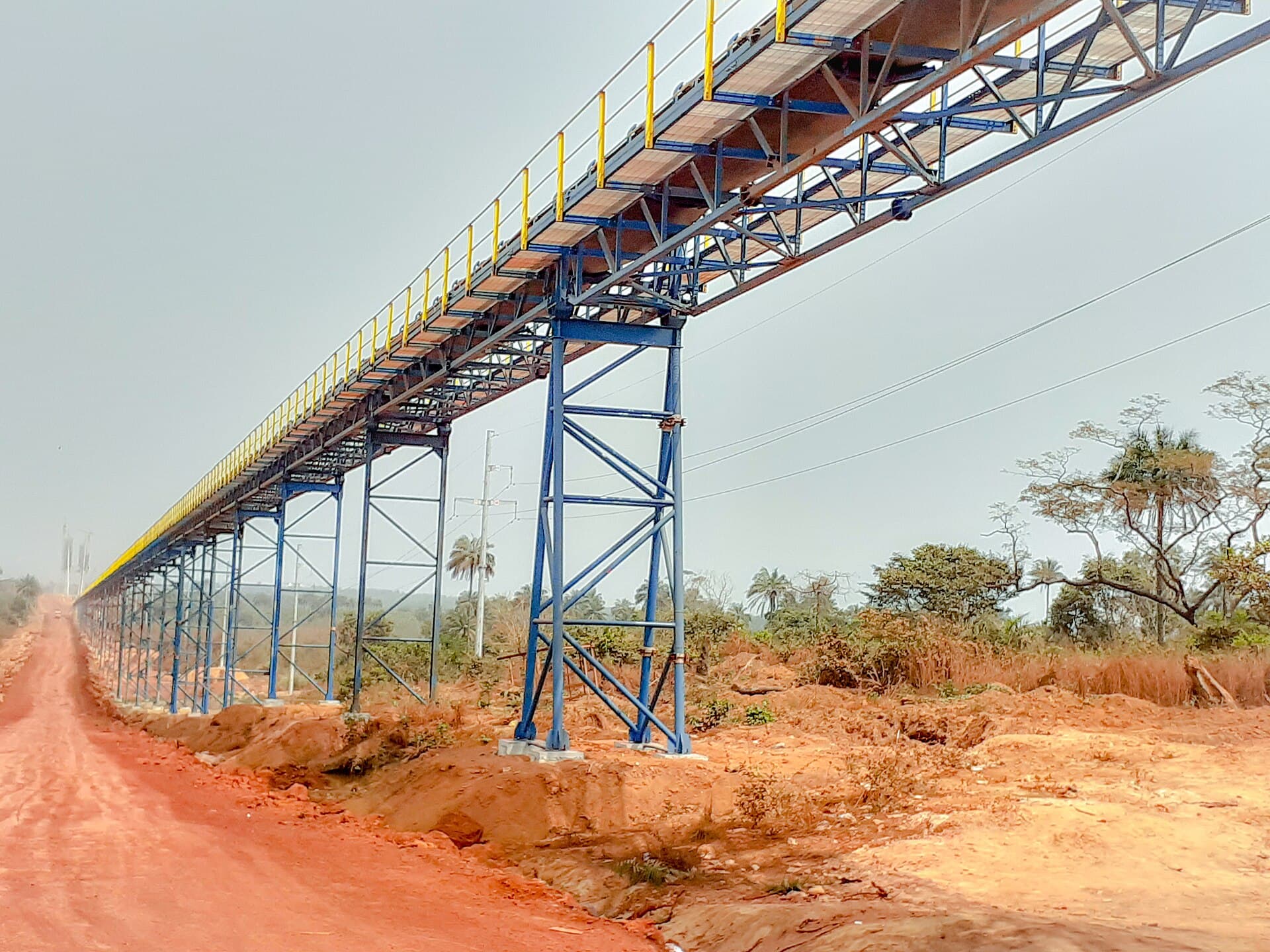 Belt conveyor carrying bauxite over a laterite track, Boffa, Guinea